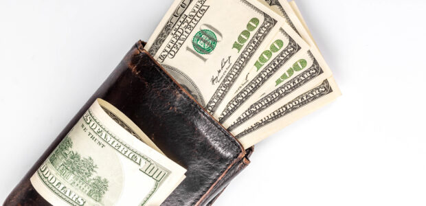 Black wallet with money inside and dollar bills on top on white background