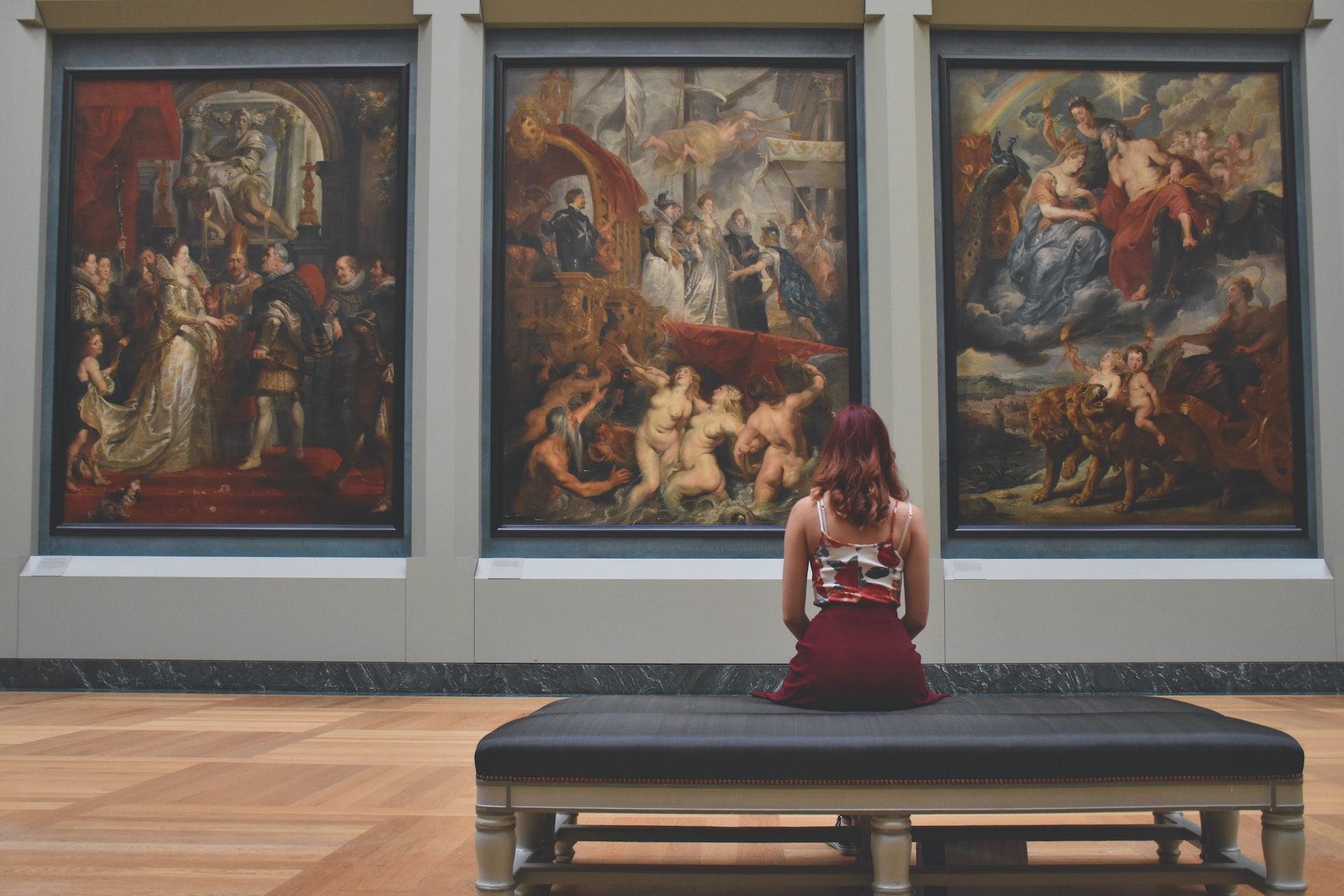 museum - Woman Sitting on Ottoman in Front of Three Paintings