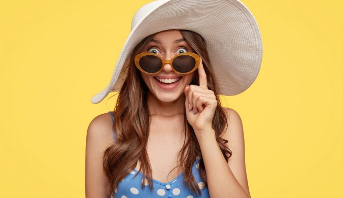 fashionable-lady-with-glad-expression-wears-white-hat-sunglasses-finds-hotel-stay-during-vacation-ready-go-beach-isolated-yellow-wall-tourism-summer-time-concept